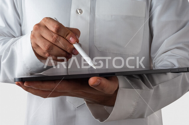 بورتريه لرجل خليجي سعودي يحمل بيده جهاز التابلت ، يستخدم القلم الخاص للضغط على شاشة الجهاز التقني ،تنظيم وادارة الاعمال عبر الجهاز التقني ، خلفية بيضاء