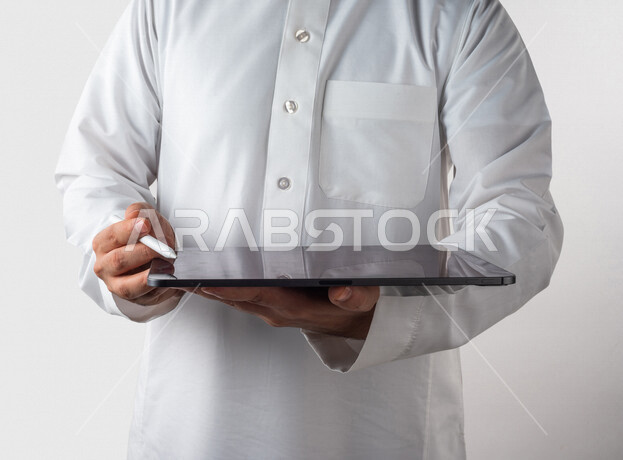 بورتريه لرجل خليجي سعودي يحمل بيده جهاز التابلت ، يستخدم القلم الخاص للضغط على شاشة الجهاز التقني ،تنظيم وادارة الاعمال عبر الجهاز التقني ، خلفية بيضاء