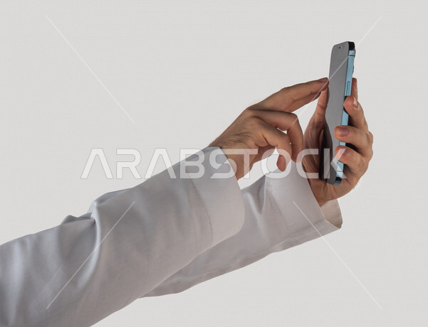 Portrait of a Saudi Gulf man holding a mobile phone, clicking on the screen, using the touch feature, using modern technical devices, white background