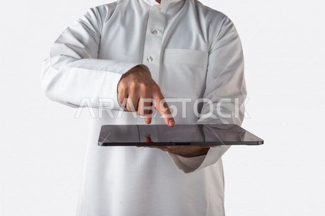 بورتريه لرجل خليجي سعودي يحمل بيده جهاز التابلت ، ينقر باصبعه على شاشة الجهاز التقني ، استخدام خاصية اللمس، استخدام اجهزة تقنية حديثة ، خلفية بيضاء