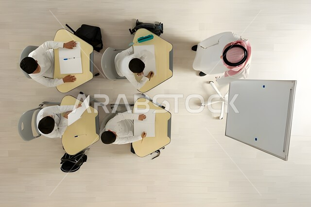 الاهتمام بتعليم الطلاب و تنمية القدرات العلمية، تأدية الواجبات المدرسية، تلاميذ عرب خليجيون سعوديون يرتدون الثوب السعودي التقليدي  يجلسون على الكراسي وأمامهم طاولات الدراسة، بورتريه علوي عامودي لمعلم عربي خليجي سعودي يقوم بإعطاء الدروس، خلفية بيج