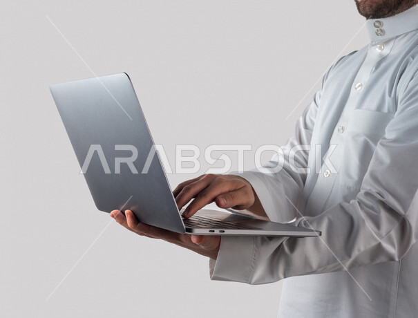 Portrait of a Saudi Gulf man holding a laptop in his hand, remote work, e-learning, using modern technical devices, white background
