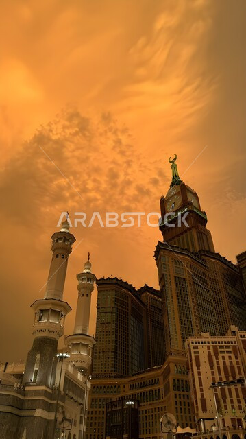 الفن الهندسي المعماري لناطحات السحاب، معالم دينية إسلامية مقدسة، صورة من الاسفل لمبنى برج الساعة الملكي في مكة المكرمة، العبادة والتقرب إلى الله، الأبراج المطلة على الحرم المكي الشريف في المملكة العربية السعودية ،منظر السماء الملبدة بالغيوم وقت غروب الشمس
