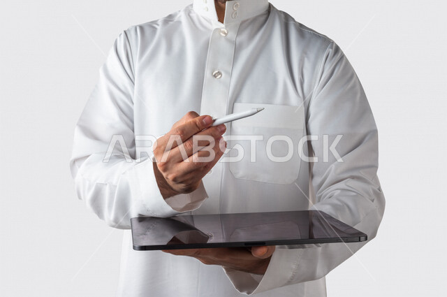 Portrait of a Saudi Gulf man holding a tablet in his hand, using the special pen to press the screen of the technical device, organizing and managing business through the technical device, white background
