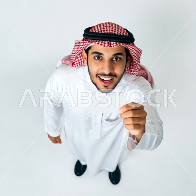 اعلانات و عروضات تسويقية, النظر الى الكاميرا بايماءات السرور السعادة، بورتريه من الاعلى لرجل عربي خليجي سعودي يرتدي الشماغ والثوب التقليدي يحمل بيده لوحة بيضاء مستطيلة، موك اب مستطيل أبيض، لوح اعلاني فارغ، صورة الجسم بالطول الكامل، خلفية بيضاء