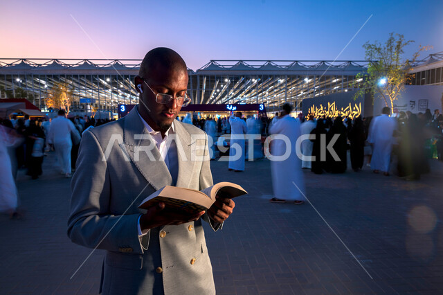 قضاء أوقات ممتعة في قراءة الكتب المفيدة للتعلم والتثقف، رجل عربي خليجي سعودي يرتدي الدلة الرسمية يقف ويحمل بيده كتاب، ممارسة هواية القراءة