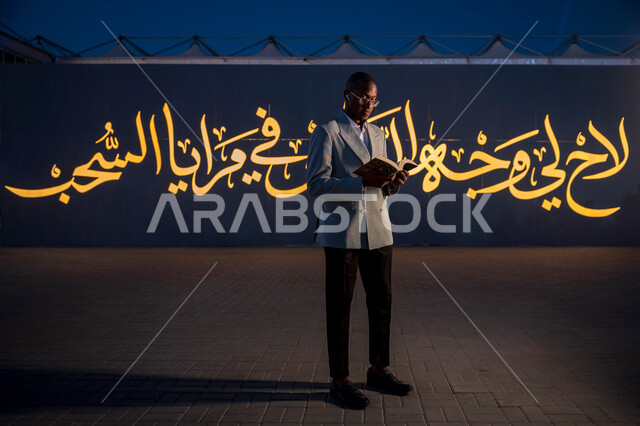 قضاء أوقات ممتعة في قراءة الكتب المفيدة للتعلم والتثقف، رجل عربي خليجي سعودي يرتدي الدلة الرسمية يقف ويحمل بيده كتاب، ممارسة هواية القراءة