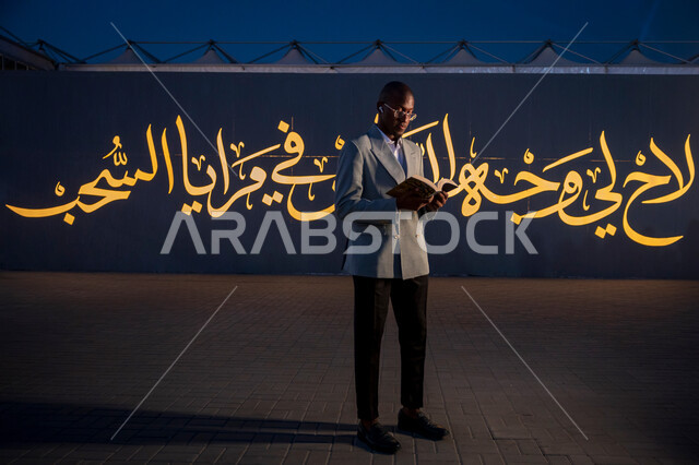 قضاء أوقات ممتعة في قراءة الكتب المفيدة للتعلم والتثقف، رجل عربي خليجي سعودي يرتدي الدلة الرسمية يقف ويحمل بيده كتاب، ممارسة هواية القراءة