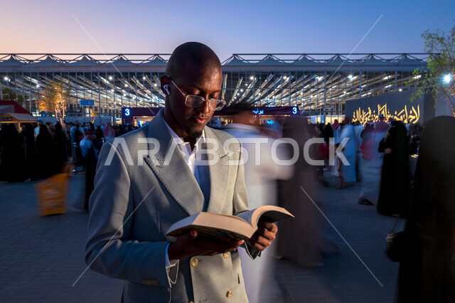 قضاء أوقات ممتعة في قراءة الكتب المفيدة للتعلم والتثقف، رجل عربي خليجي سعودي يرتدي الدلة الرسمية يقف ويحمل بيده كتاب، ممارسة هواية القراءة