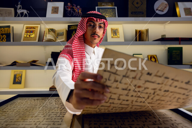 ممارسة هواية المطالعة, قضاء أوقات ممتعة في تصفح الكتب المفيدة للتعلم والتثقف، شاب عربي سعودي خليجي يرتدي الثوب مع الشماغ و يقف في معرض الكتاب يقوم بالقراءة