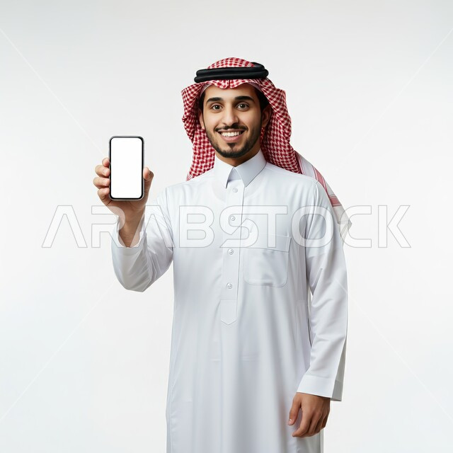 عرض التطبيقات والخدمات الحديثة، بورتريه لشاب عربي خليجي سعودي مبتسم يرتدي الثوب التقليدي والشماغ يقوم بعرض شاشة بيضاء فارغة عبر الهاتف المحمول ينظر إلى الكاميرا بإيماءات السرور، استخدام التكنولوجيا المتطورة للتسويق الرقمي الإلكتروني، خلفية بيضاء