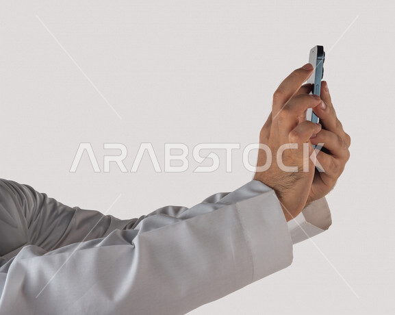 بورتريه لرجل خليجي سعودي يحمل بيده الهاتف المحمول النقر بالاصبع على الشاشة ،استخدام خاصية اللمس، استخدام اجهزة تقنية حديثة ،  خلفية بيضاء