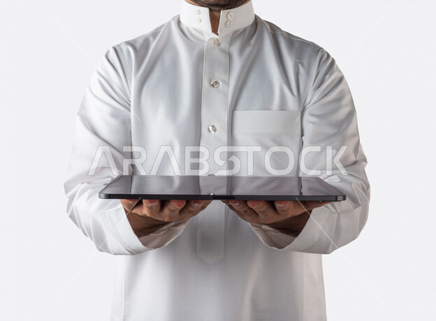 بورتريه لرجل خليجي سعودي يحمل بيده جهاز التابلت ، استخدام اجهزة تقنية حديثة ، خلفية بيضاء