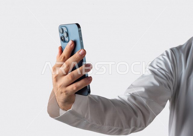 بورتريه لرجل خليجي سعودي يحمل بيده الهاتف المحمول ، اجراء اتصال فيديو ،تصوير سيلفي ،استخدام اجهزة تقنية حديثة ،  خلفية بيضاء