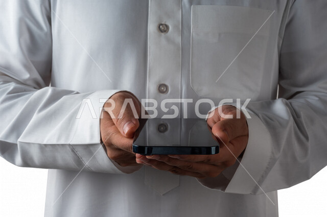 بورتريه لرجل خليجي سعودي يحمل بيده الهاتف المحمول ، اجراء اتصال فيديو ،تصوير سيلفي ،استخدام اجهزة تقنية حديثة ،  خلفية بيضاء