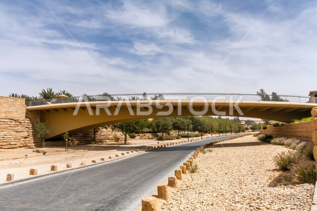 الطرق والشوارع العامة في مدينة الرياض، الاشجار والنباتات الخضراء على الجبال في وضح النهار، جسر للمشاة عبر وادي حنيفة بالقرب من قلعة الدرعية التاريخية، الغيوم والسحب البيضاء في سماء المملكة، المناظر الطبيعية في السعودية