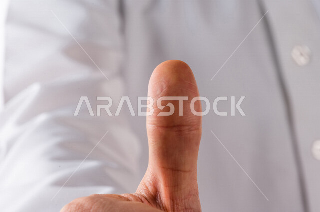 بورتريه لرجل خليجي سعودي يرتدي الزي الخليجي التقليدي يقوم بايماءات يد مختلفة ، يرفع اصبع الابهام لاعلى لاعجابه بشيء ما ، خلفية بيضاء