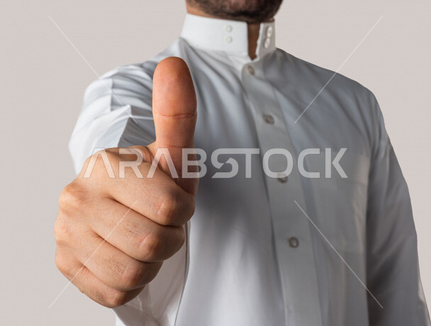 بورتريه لرجل خليجي سعودي يرتدي الزي الخليجي التقليدي يقوم بايماءات يد مختلفة ، يرفع اصبع الابهام لاعلى لاعجابه بشيء ما ، خلفية بيضاء