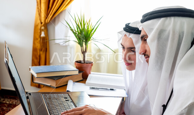 مفهوم التعليم عبر الانترنت, شابان عربيان سعوديان خليجيان يدرسان في المنزل باستخدام جهاز الحاسب المحمول، متابعة حصص الاونلاين، التعلم عن بعد، الدراسة من خلال منصة تعليمية