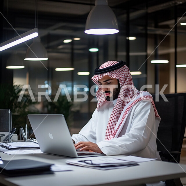 إدارة شؤون الأعمال وتنظيمها عبر الاجهزة التقنية، مهن ووظائف ادارية مكتبية، دمج العمل مع التقنية والتكنولوجيا، رجل اعمال عربي خليجي سعودي يرتدي الثوب ويضع الشماغ والعقال, العمل على الحاسوب المحمول داخل المكتب