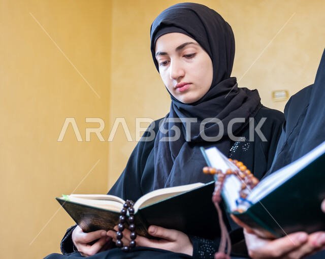 الاجتهاد في الطاعات والأدعية والأذكار, فضل وثواب حفظ القرآن الكريم، التعبد في بيوت الله عز وجل، مفهوم العبادة والتقرب من الله تعالى، أجواء دينية روحانية، شابة عربية خليجية سعودية ترتدي العباءة السوداء تقوم بقراءة المصحف الشريف بايماءات التركيز