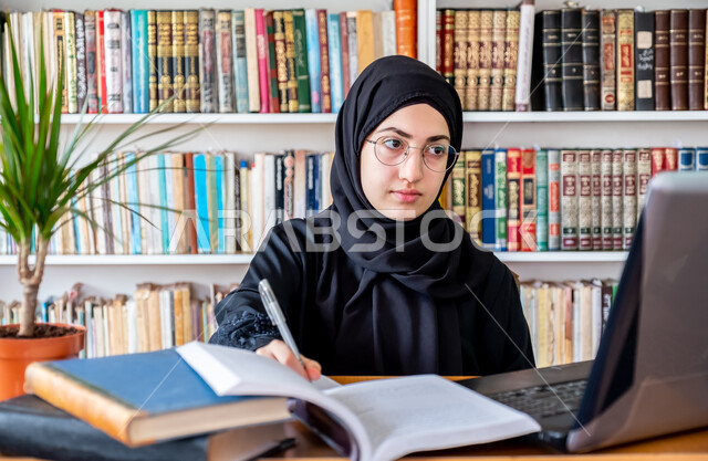 المناهج والمواد التعليمية في السعودية، مفهوم الثقافة والتعلم الذاتي , صورة مقربة لشابة عربية خليجية سعودية محجبة مبتسمة ترتدي عباءة سوداء تقوم بمتابعة الدراسة عبر الحاسب، استخدام الأجهزة التقنية الحديثة لحضور المحاضرات الجامعية، التعليم عن بعد عن طريق الانترنت
