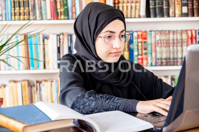 Higher education in Saudi colleges, the concept of culture and self-learning, writing scientific reports and research, a young Saudi Arabian Gulf woman sitting in the university library and using a laptop to review daily lessons, electronic university lectures and distance learning