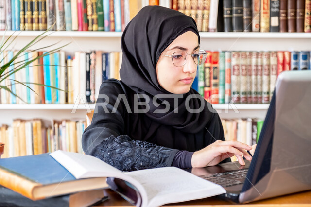 كتابة التقارير والأبحاث العلمية، شابة عربية خليجية سعودية تجلس في مكتبة الجامعة وتستخدم الحاسوب المحمول في مراجعة الدروس اليومية، الإستعداد للمحاضرات الجامعية الإلكترونية والتعلم عن بعد، التعليم العالي في الكليات السعودية، مفهوم الثقافة والتعلم الذاتي