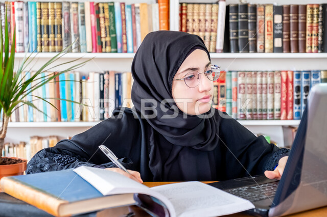 المناهج والمواد التعليمية في السعودية، مفهوم الثقافة والتعلم الذاتي , صورة مقربة لشابة عربية خليجية سعودية محجبة مبتسمة ترتدي عباءة سوداء تقوم بمتابعة الدراسة عبر الحاسب، استخدام الأجهزة التقنية الحديثة لحضور المحاضرات الجامعية، التعليم عن بعد عن طريق الانترنت