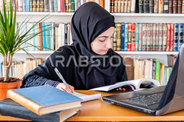 التعليم عن بعد عن طريق الانترنت، المناهج والمواد التعليمية في السعودية، مفهوم الثقافة والتعلم الذاتي , صورة مقربة لشابة عربية خليجية سعودية محجبة ترتدي عباءة سوداء تقوم بمتابعة الدراسة عبر الحاسب، استخدام الأجهزة التقنية الحديثة لحضور المحاضرات الجامعية