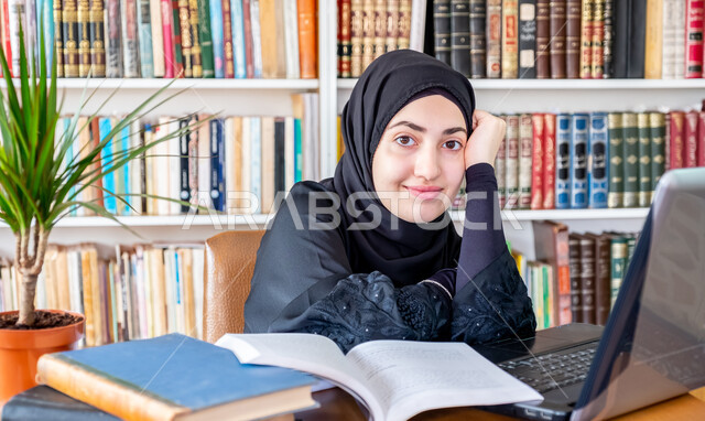 مفهوم الثقافة والتعلم الذاتي , صورة مقربة لشابة عربية خليجية سعودية محجبة مبتسمة ترتدي عباءة سوداء تنظر الى الكاميرا بايماءات السعادة، استخدام الأجهزة التقنية الحديثة لمتابعة المحاضرات الجامعية، التعليم عن بعد، المناهج و المواد التعليمية في السعودية