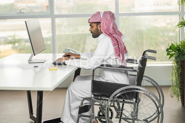 A Saudi Arabian Gulf employee of people of determination working on a computer in the workplace, integrating and employing people with disabilities in various fields, social empowerment, interest and support of the Saudi community for people with special