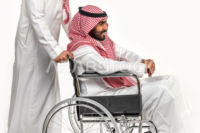 بورتريه لرجل عربي سعودي خليجي من ذوي الهمم يجره صديقه على كرسي متحرك, التمكين الاجتماعي, اهتمام  ودعم المجتمع السعودي لذوي الاحتياجات الخاصه, شعور ذوي الهمم بالراحه والطمأنينه في بيئتهم