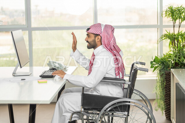 موظف عربي سعودي خليجي من ذوي الهمم يعمل على جهاز الحاسوب في مقر العمل, دمج و توظيف ذوي الاعاقه في مختلف المجالات, التمكين الاجتماعي, اهتمام  ودعم المجتمع السعودي لذوي الاحتياجات الخاصه, شعور ذوي الهمم بالراحه والطمأنينه في بيئتهم, اجتماع عمل عن بعد عبر ال