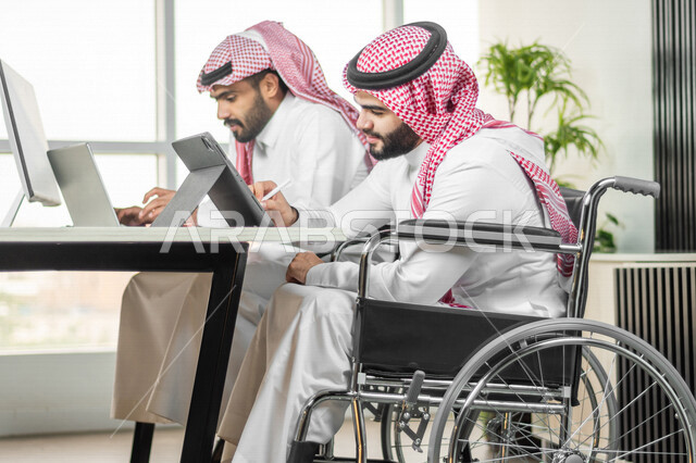 موظف عربي سعودي خليجي من ذوي الهمم يعمل على جهاز التابلت في مقر العمل, دمج و توظيف ذوي الاعاقه في مختلف المجالات, التمكين الاجتماعي, اهتمام  ودعم المجتمع السعودي لذوي الاحتياجات الخاصه, شعور ذوي الهمم بالراحه والطمأنينه في بيئتهم