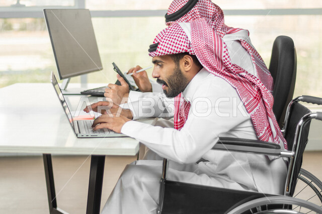 موظف عربي سعودي خليجي من ذوي الهمم يعمل على جهاز الحاسوب في مقر العمل, دمج و توظيف ذوي الاعاقه في مختلف المجالات, التمكين الاجتماعي, اهتمام  ودعم المجتمع السعودي لذوي الاحتياجات الخاصه, شعور ذوي الهمم بالراحه والطمأنينه في بيئتهم