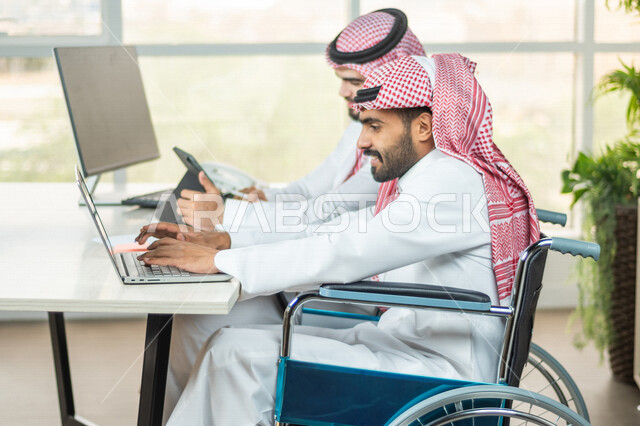 موظف عربي سعودي خليجي من ذوي الهمم يعمل على جهاز الحاسوب في مقر العمل, دمج و توظيف ذوي الاعاقه في مختلف المجالات, التمكين الاجتماعي, اهتمام  ودعم المجتمع السعودي لذوي الاحتياجات الخاصه, شعور ذوي الهمم بالراحه والطمأنينه في بيئتهم