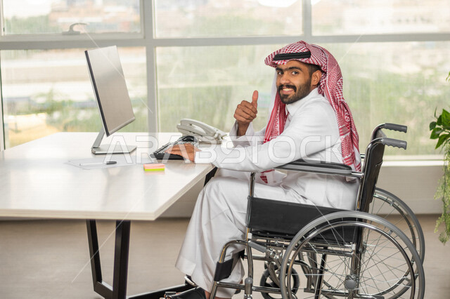 موظف عربي سعودي خليجي من ذوي الهمم يعمل على جهاز الحاسوب في مقر العمل, دمج و توظيف ذوي الاعاقه في مختلف المجالات, التمكين الاجتماعي, اهتمام  ودعم المجتمع السعودي لذوي الاحتياجات الخاصه, شعور ذوي الهمم بالراحه والطمأنينه في بيئتهم