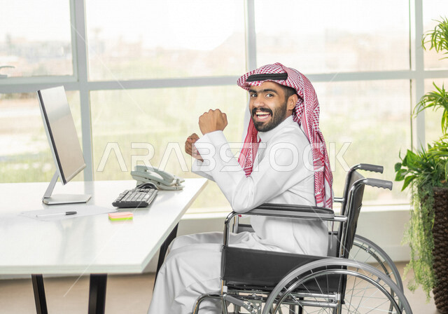 موظف عربي سعودي خليجي من ذوي الهمم يعمل على جهاز الحاسوب في مقر العمل, دمج و توظيف ذوي الاعاقه في مختلف المجالات, التمكين الاجتماعي, اهتمام  ودعم المجتمع السعودي لذوي الاحتياجات الخاصه, ايماءات وتعابير وجه ويدين تدل على الفوز والنجاح