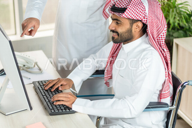 موظف عربي سعودي خليجي من ذوي الهمم يعمل على جهاز الحاسوب في مقر العمل, دمج و توظيف ذوي الاعاقه في مختلف المجالات, التمكين الاجتماعي, اهتمام  ودعم المجتمع السعودي لذوي الاحتياجات الخاصه, شعور ذوي الهمم بالراحه والطمأنينه في بيئتهم