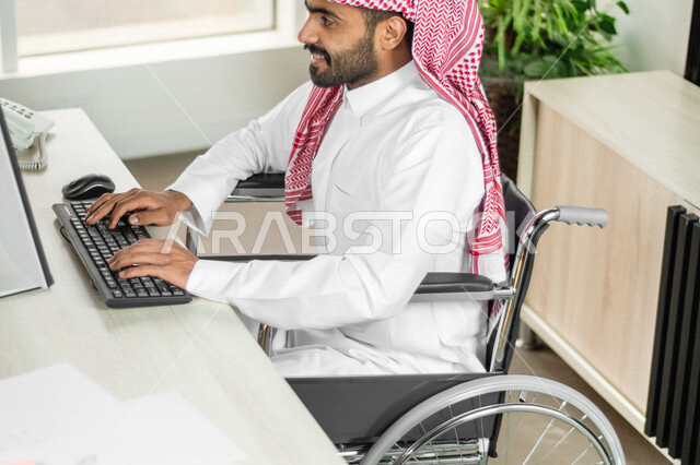 موظف عربي سعودي خليجي من ذوي الهمم يعمل على جهاز الحاسوب في مقر العمل, دمج و توظيف ذوي الاعاقه في مختلف المجالات, التمكين الاجتماعي, اهتمام  ودعم المجتمع السعودي لذوي الاحتياجات الخاصه, شعور ذوي الهمم بالراحه والطمأنينه في بيئتهم
