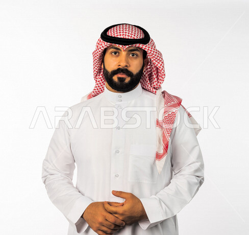 بورتريه لرجل سعودي خليجي يقوم بجلسة تصوير، ينظر إلى الكاميرا بإيماءات وجه ويدين مختلفة ، خلفية بيضاء لرجل سعودي مسلم يرتدي زي تقليدي سعودي مع شماغ وعقال