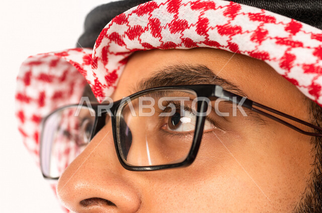 بورتريه بصورة مقربة لرجل سعودي خليجي يقوم بجلسة تصوير ، ينظر لأعلى ، خلفية بيضاء لرجل سعودي مسلم يرتدي زي تقليدي سعودي مع شماغ وعقال