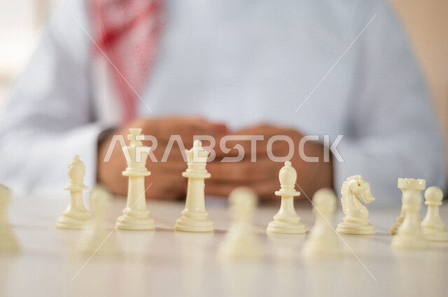 صورة مقربة ليد رجل سعودي خليجي يلعب لعبة الشطرنج ، مفهوم التركيز والتحدي ، التسليه والترفيه ، لعبة شطرنج على طاولة بيضاء ، مفهوم التخطيط والتفكير في استراتيجية مناسبة