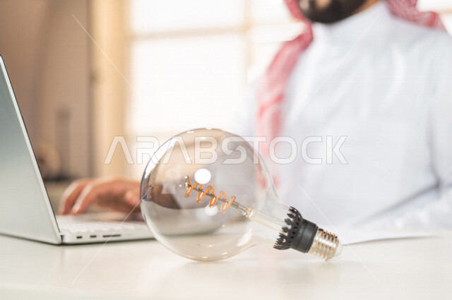 صورة مقربة لرجل سعودي خليجي على المكتب، إستخدام جهاز الحاسوب المحمول لإنجاز المهام ، أفكار إبداعية تطويرية، مفهوم الفكرة مع الإبتكار والإلهام، تحقيق الإنجازات والإبتكارات ، براءة الإختراع ، المصباح الكهربائي الضوئي، العمل عن بعد، التسويق الإلكتروني
