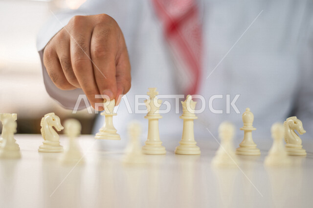 صورة مقربة ليد رجل سعودي خليجي يلعب لعبة الشطرنج ، مفهوم التركيز والتحدي ، التسليه والترفيه ، لعبة شطرنج على طاولة بيضاء ، مفهوم التخطيط والتفكير في استراتيجية مناسبة