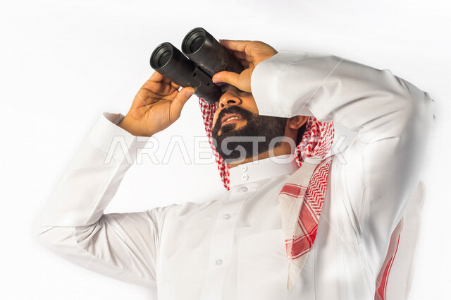 بورتريه لرجل سعودي خليجي يقوم بالنظر من خلال المنظار ثنائي العينين (التلسكوب) بإيماءات وجه ويدين مختلفة ، خلفية بيضاء لرجل سعودي مسلم يرتدي زي تقليدي سعودي مع شماغ وعقال