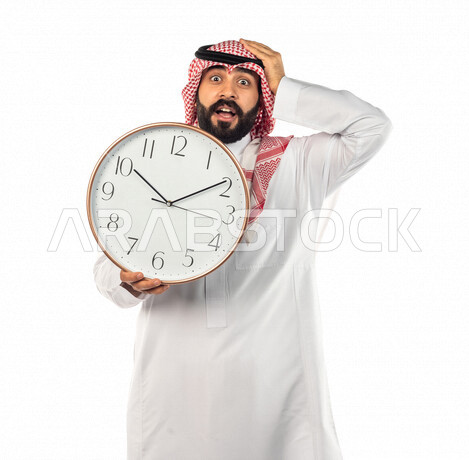 بورتريه لرجل سعودي خليجي يحمل ساعة رقمية كبيرة بإيماءات وجه ويدين مختلفة ، خلفية بيضاء لرجل سعودي يرتدي الزي التقليدي السعودي مع شماغ وعقال ، مفهوم العد التنازلي ، الدقة في المواعيد ، التذكيرات والتنبيهات الثابته ، مواعيد العمل ، إنجاز المهامات في الوقت