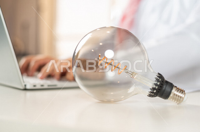 صورة مقربة لرجل سعودي خليجي على المكتب، إستخدام جهاز الحاسوب المحمول لإنجاز المهام ، أفكار إبداعية تطويرية، مفهوم الفكرة مع الإبتكار والإلهام، تحقيق الإنجازات والإبتكارات ، براءة الإختراع ، المصباح الكهربائي الضوئي، العمل عن بعد، التسويق الإلكتروني
