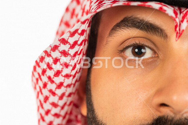 بورتريه بصورة مقربة لرجل سعودي خليجي يقوم بجلسة تصوير ، ينظر لأعلى ، خلفية بيضاء لرجل سعودي مسلم يرتدي الزي التقليدي السعودي مع شماغ وعقال